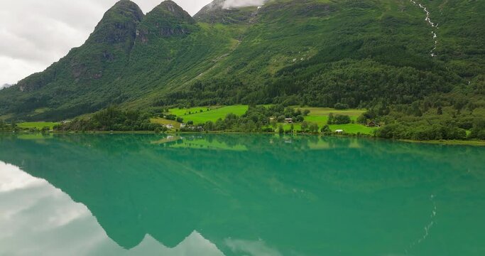 Aerial parallax around Oldevatnet glacial lake water reflecting forested mountain above, Norway