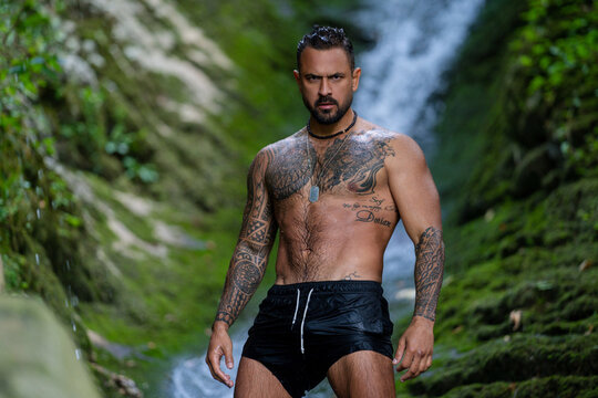 Man near waterfall. Man freedom lifestyle. Tourism in nature. Hispanic man tourist. Lifestyle relaxation concept, summer travel on nature. Naked Man under the waterfall enjoying splashing.