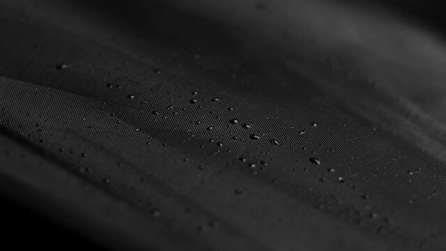 Raindrops on the black material of a closed umbrella. Wet dark textile with water drops. Rainy season concept. Rotation