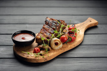 hot grilled spare ribs from a summer BBQ served with a grilled vegetables and sauce on an old vintage wooden cutting board