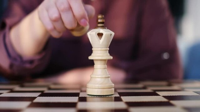 A woman's hand thoughtfully replaces a queen with a pawn on the chessboard, a deliberate strategy that evokes the nuanced tactics of understatement and patience.