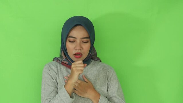 young Asian muslim woman in gray cloth feeling unwell and coughing isolated over green background. People religious lifestyle concept
