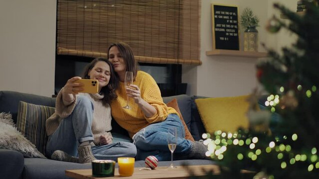 A young lesbian couple spends time together during the Christmas holidays. Two women take selfies on the phone while sitting on the couch in the living room.