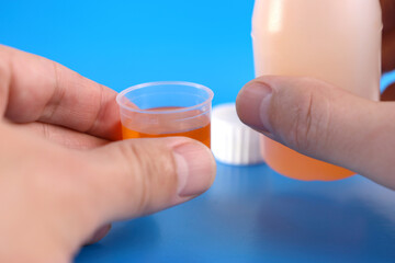 Medicinal syrup is poured into a vessel with liquid volume divisions on a blue background....