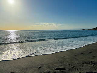 大きな海に波が打ち寄せ、青い大空と太陽と夕日が混ざり合い、高台から見下ろす実写写真