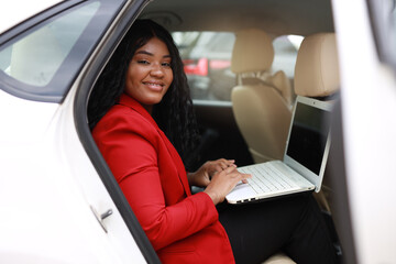 beautiful african passenger in the back seat of a car with a laptop