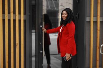 joyful african woman in a red jacket opens the door of the house