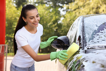 Happy woman washing car with sponge outdoors