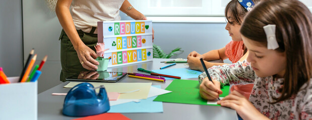 Unrecognizable female teacher holding lightbox with text reduce, reuse, recycle while young...