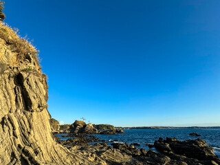 大きな海に波が打ち寄せ、青い大空と太陽と夕日が混ざり合い、高台から見下ろす実写写真