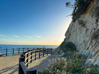 Obraz premium 大きな海に波が打ち寄せ、青い大空と太陽と夕日が混ざり合い、高台から見下ろす実写写真