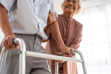 Asian attractive senior woman support elderly man walking with walker.