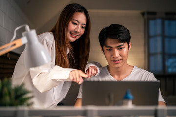 Asian young man overworking at home at night in bedroom with his wife. 