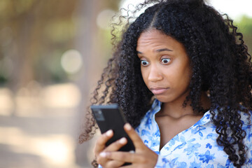 Perplexed black woman checking phone in a park