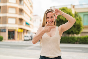 Young blonde woman at outdoors focusing face. Framing symbol