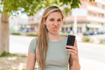 Young blonde woman using mobile phone at outdoors with sad expression