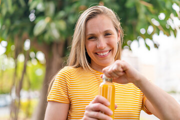 Young blonde woman holding an orange juice at outdoors