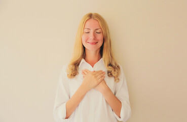 Portrait of beautiful happy smiling caucasian grateful woman put folded hands on her heart on white studio background