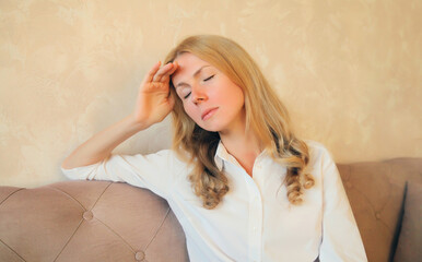 Sad tired caucasian young woman with headache or temples pain sitting on the couch in the room at...