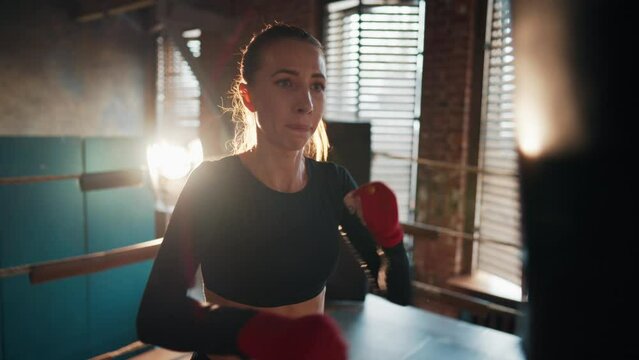 Young strong woman boxer in sportswear gives punches by hans on boxing ring. Training, workout and professional sport concept. Self-defence, girls power, womans power and prepares to fight, feminism.