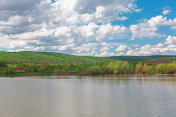 Landscape with a lake in the middle of the forest and clouds . Springtime rustic scenery 