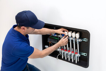 An air conditioning technician is adjusting an electronic head of an underfloor heating manifold