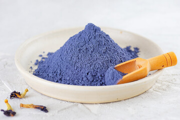 Blue matcha powder from clitoria flowers with wooden scoop in a light plate.