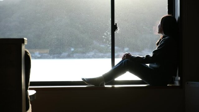 A woman sitting by the window and looking at sea view