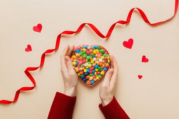 Female hands with delicious candies in box on color background