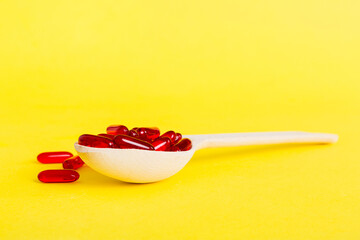 Vitamin capsules in a spoon on a colored background. Pills served as a healthy meal. Red soft gel vitamin supplement capsules on spoon