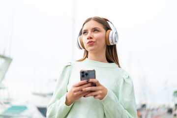 Young pretty blonde woman listening music with a mobile and thinking