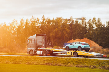 A rollback tow truck transports a broken car on the public road. Car failure during the journey....