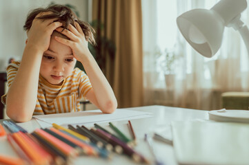 Depressed boy with paper and pencils sitting at desk