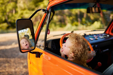 Girl sticking out tongue looking in side view mirror of caravan