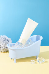 A mini bathtub filled with ice and a tube of facial cleanser. Fresh space with two main colors beige and blue. Cosmetic mockup for advertising.