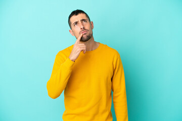 Young handsome caucasian man isolated on blue background having doubts while looking up