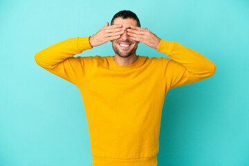 Young handsome caucasian man isolated on blue background covering eyes by hands and smiling