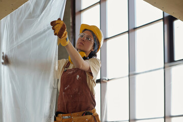 Young construction worker hanging plastic foil at site