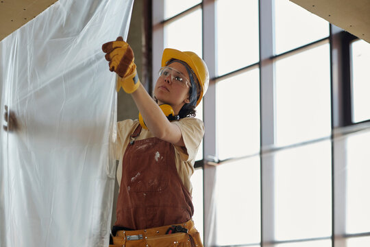 Young construction worker hanging plastic foil at site
