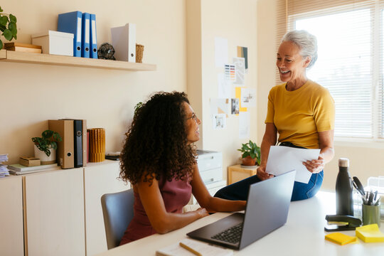 Smiling businesswoman talking to colleague with laptop on table in office