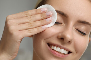 Smiling woman removing makeup with cotton pad on blurred background, closeup