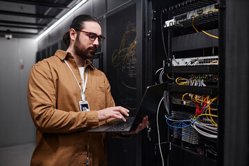 Young IT engineer using laptop and setting computer network in data room