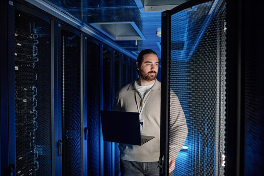 Engineer holding laptop and examining supercomputer in server room