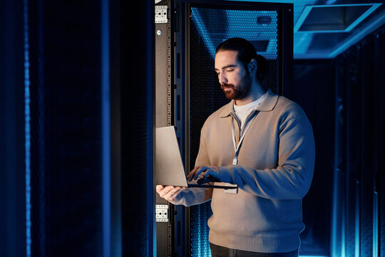 IT professional working on laptop and standing near server rack