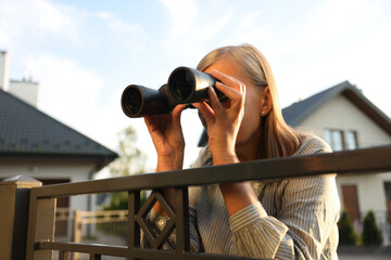 Concept of private life. Curious senior woman with binoculars spying on neighbours over fence outdoors - obrazy, fototapety, plakaty