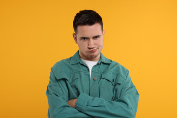 Portrait of resentful man with crossed arms on orange background