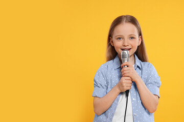 Cute little girl with microphone singing on yellow background, space for text