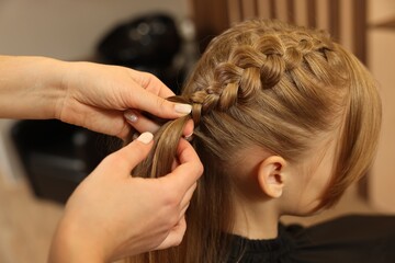 Professional hairdresser braiding girl's hair in beauty salon, closeup