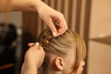 Naklejka premium Professional hairdresser braiding girl's hair in beauty salon, closeup