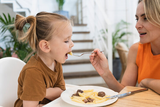Mother feeding pasta to boy at dining table at home
